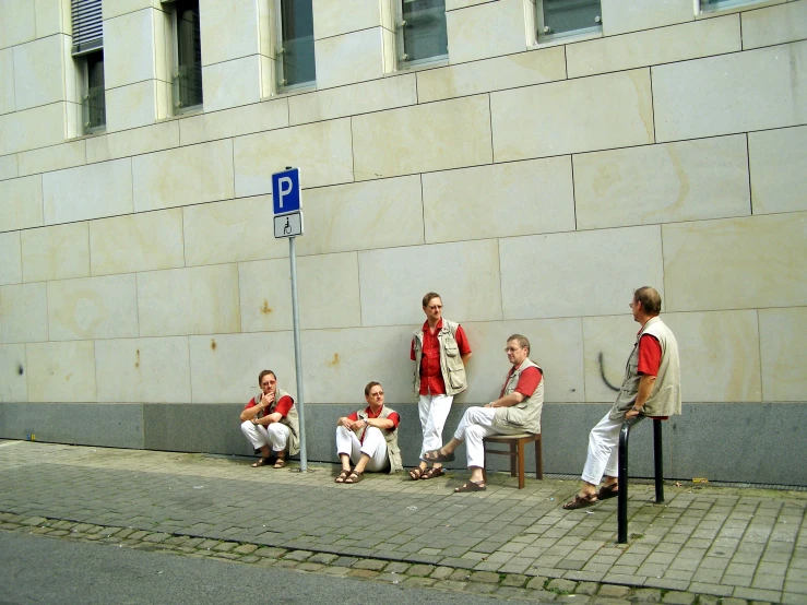 a group of men sitting outside next to a wall