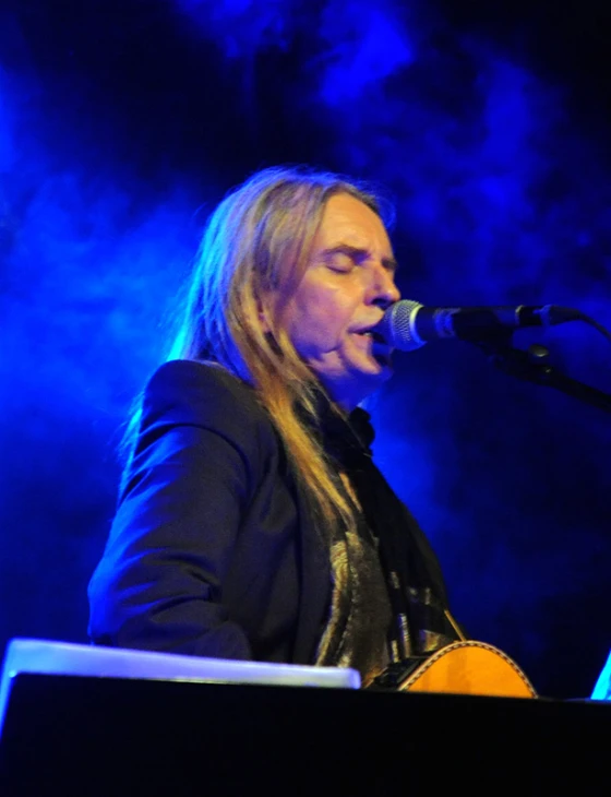 a man with long blonde hair singing on stage