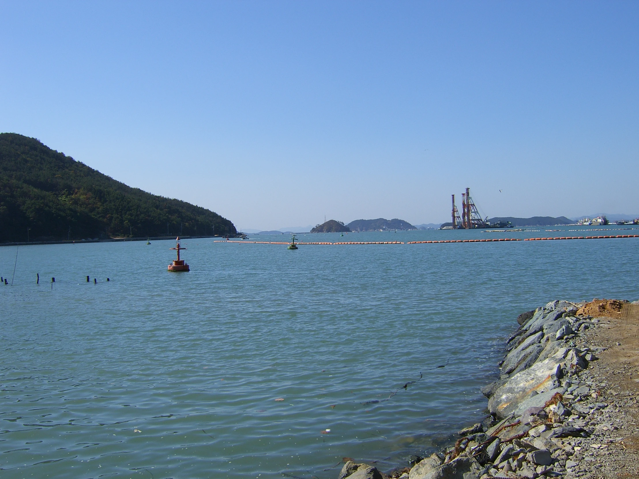 a body of water next to a large hill covered in a forest