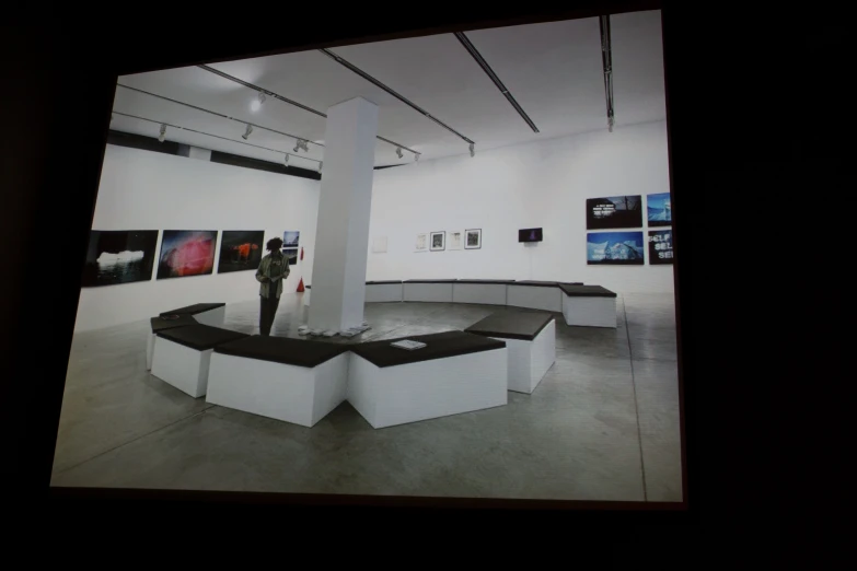 a po taken on a television screen shows a person standing on a pedestal in an art gallery