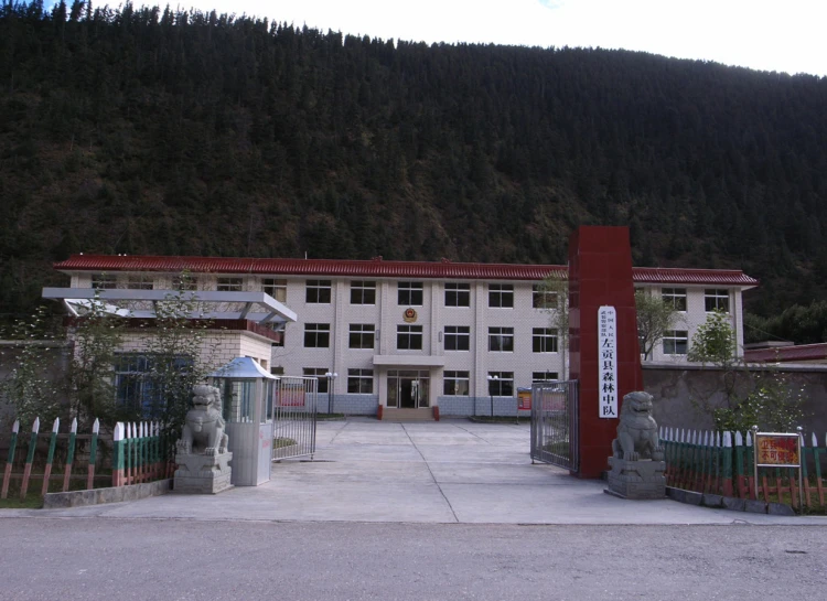 two people are in front of a large building with trees in the background