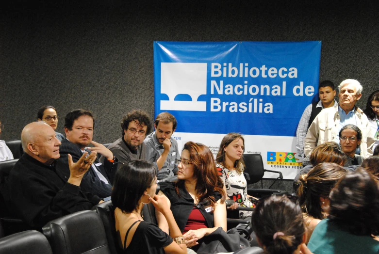 people watching an event in a dark room with a large blue sign