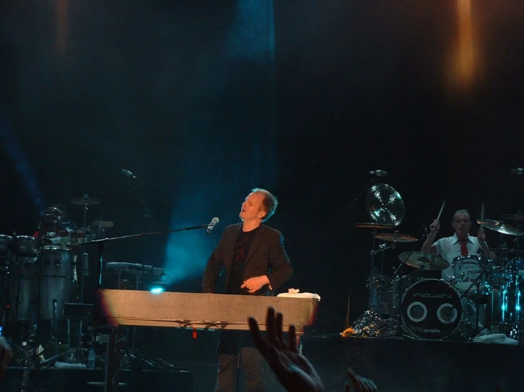 a man on stage playing a keyboard with the people in front