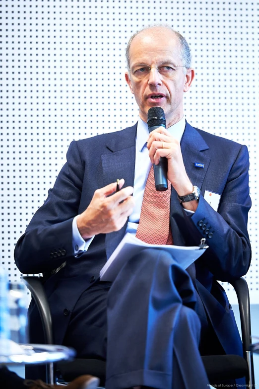 an older man speaking into a microphone while seated down