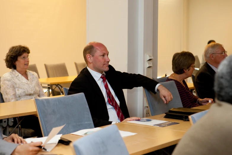 people in a room with desks and one man has his hand out