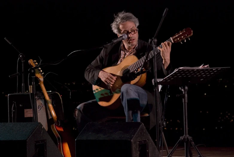 a man playing a song while sitting on stage with other instruments