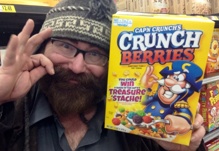 a bearded man standing next to a yellow cereal box