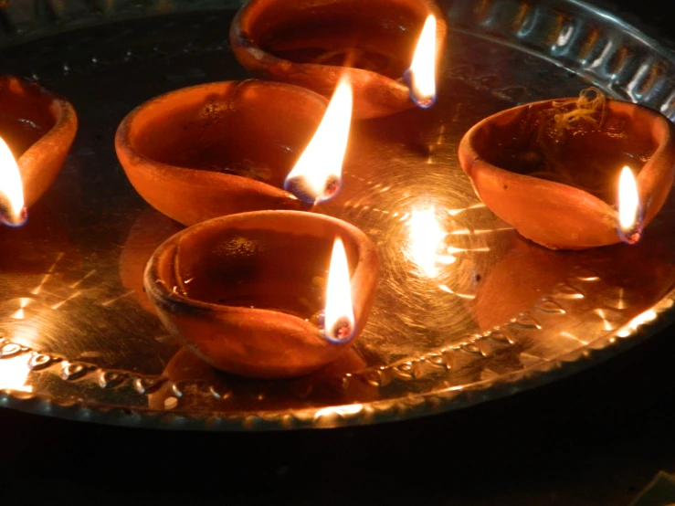 five lit candles in a small, metal bowl