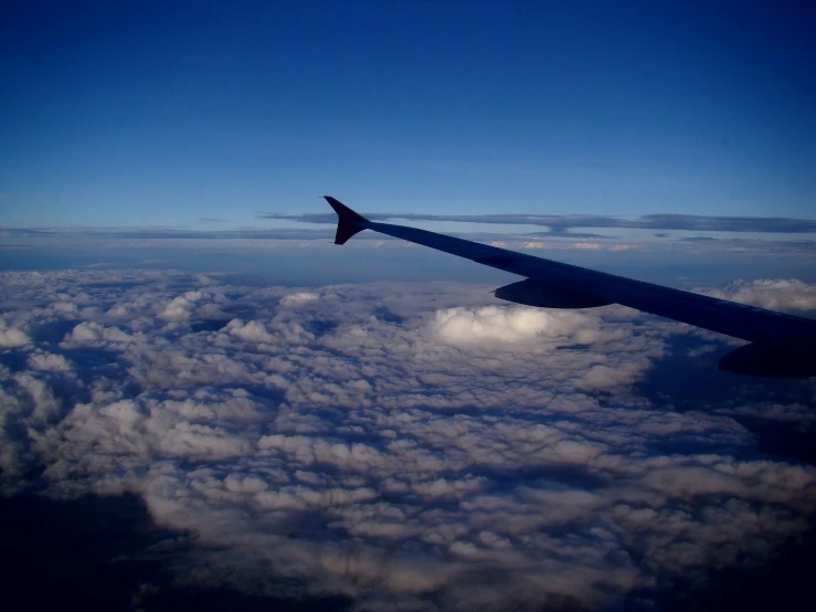 a view of the wing and part of a plane in the air above the clouds