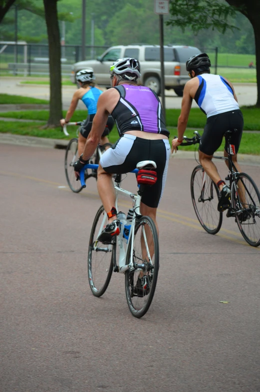 three bicyclists wearing various colored jerseys, riding down the street