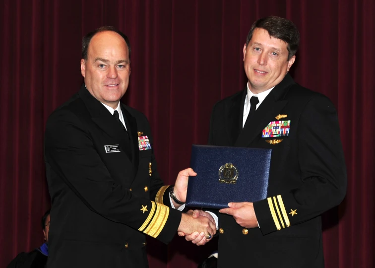 two men in navy uniforms and one is holding an award