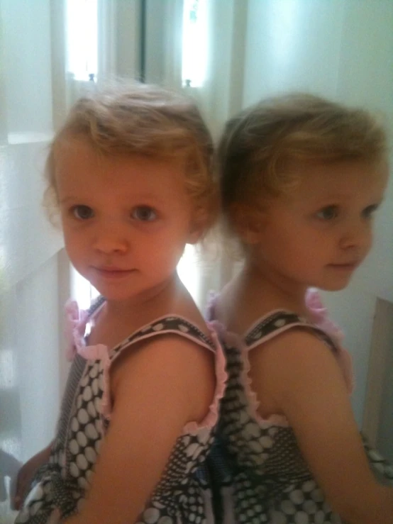 two little girls sitting next to each other near a mirror