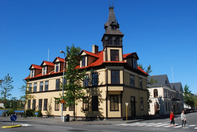 a large building with red roofing and two people walking by