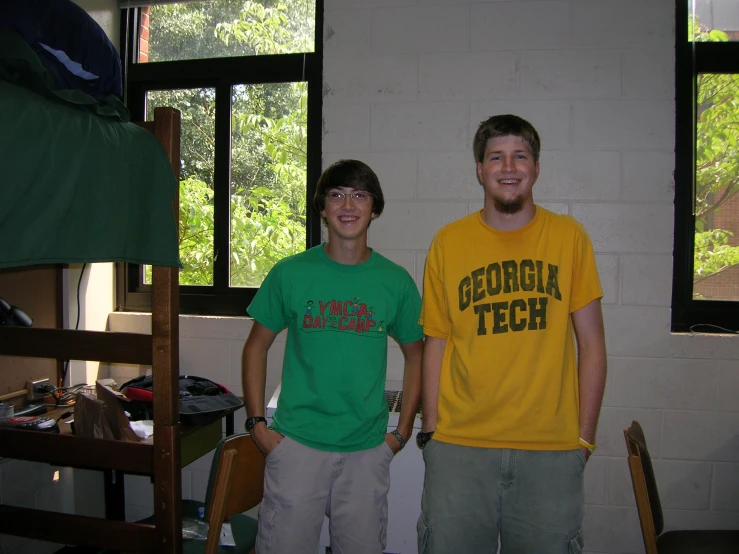 two young men stand in a dorm room with bunk beds