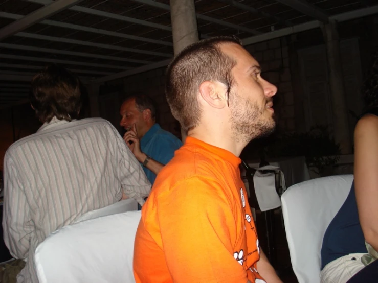 a man wearing an orange shirt looks to his left