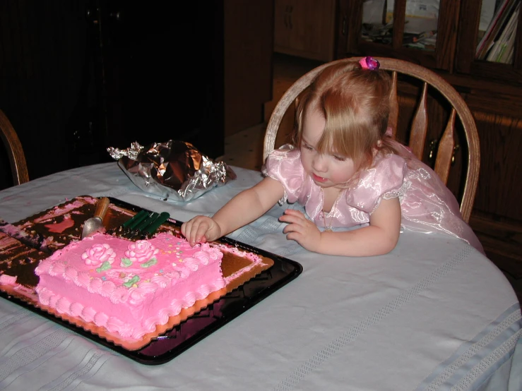a little girl with red hair wearing a pink dress is next to a square cake on a table