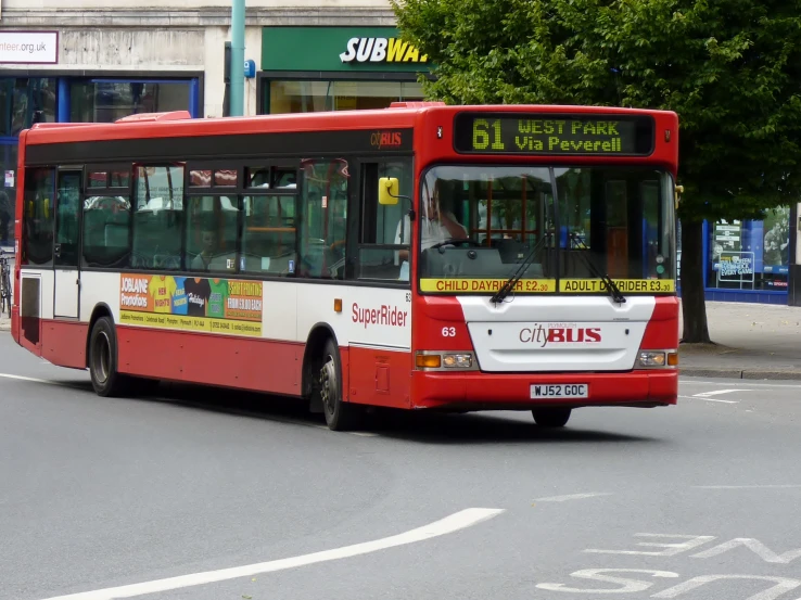 a red bus traveling down the street past stores