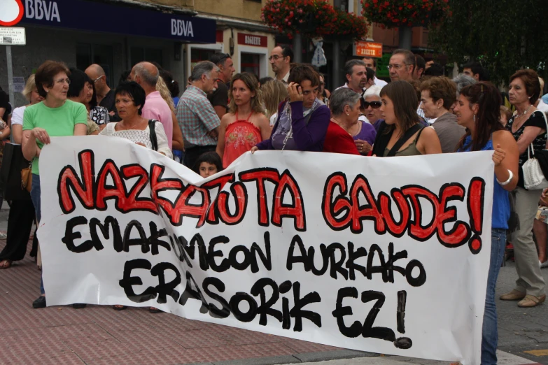 people standing around a protest sign with black and red writing