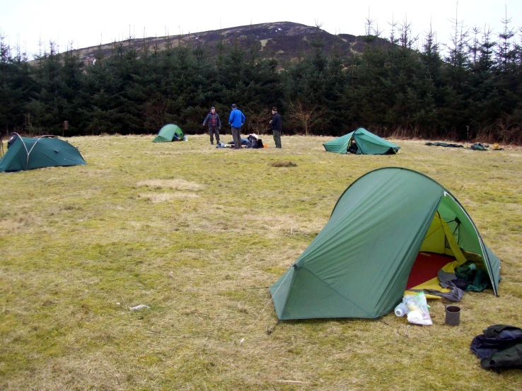 the four people are standing in the field near the green tents