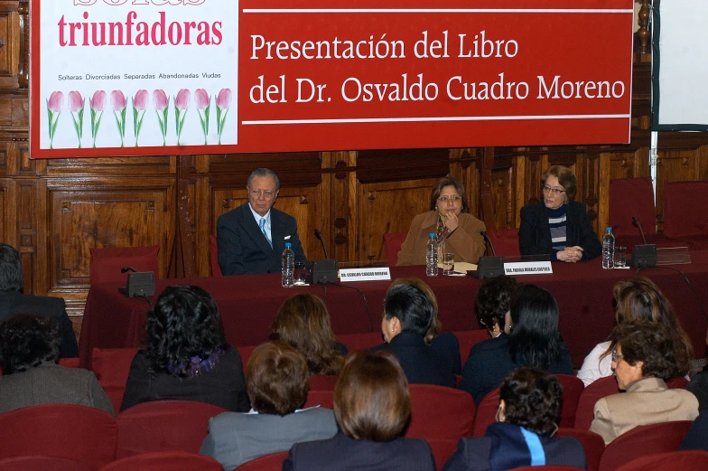 three people at a panel for an event sitting on red chairs