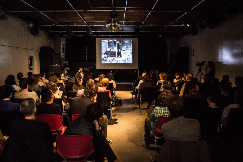 a group of people sitting in chairs facing away from the room while a screen is projected