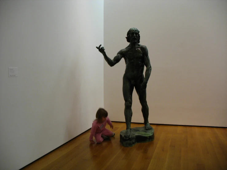 small child sitting on the ground next to a statue