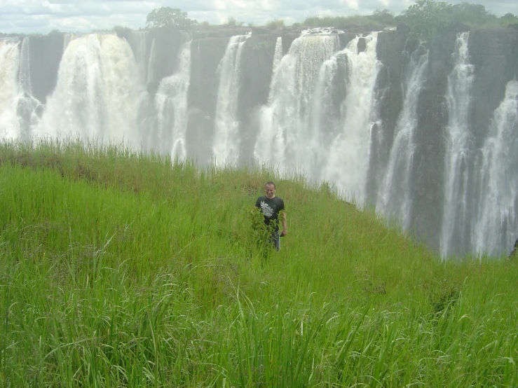 a man in front of a waterfall that has tall green grass and is looking at the camera