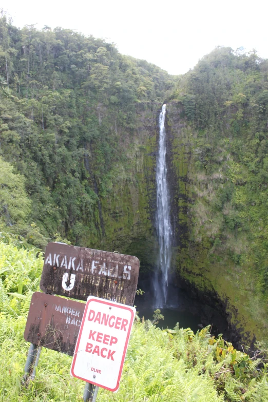 a sign with a danger sign on it and a small waterfall behind