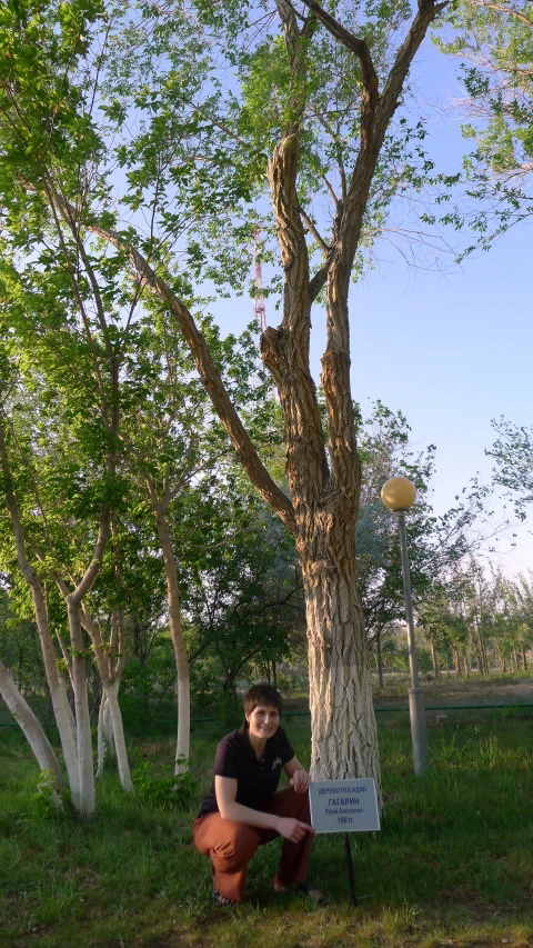 man crouched near a tree in front of a sign