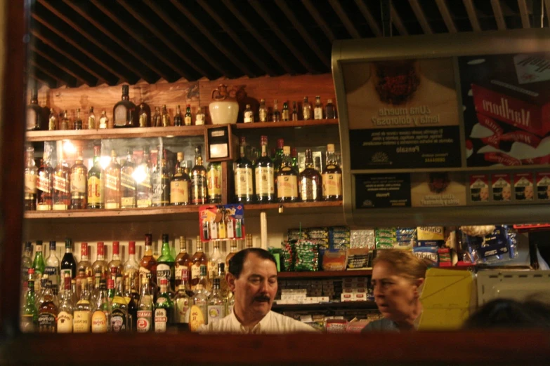 the two men are sitting at the bar, in front of bottles