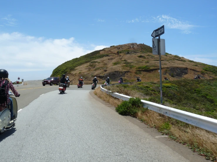 a motorcycle with people riding down the road near a hill
