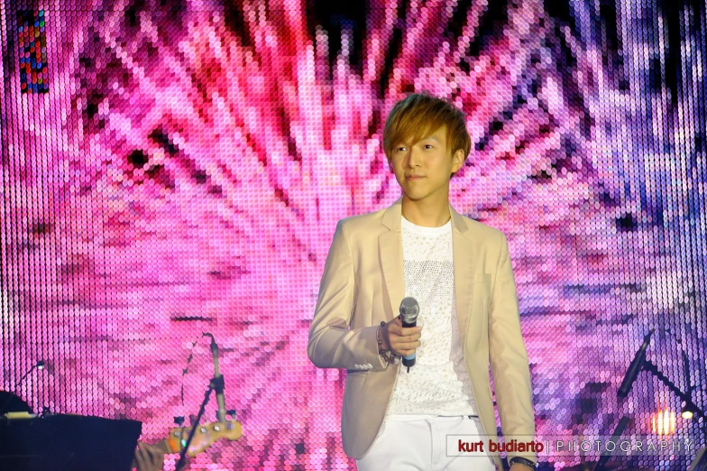asian man holding microphone on stage with large screen in background