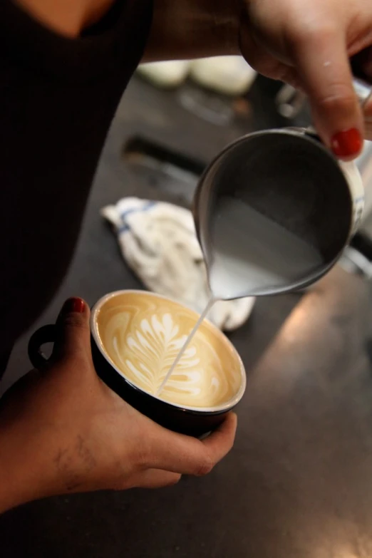 a cup of coffee with a frothy topping being stirred by a female hand