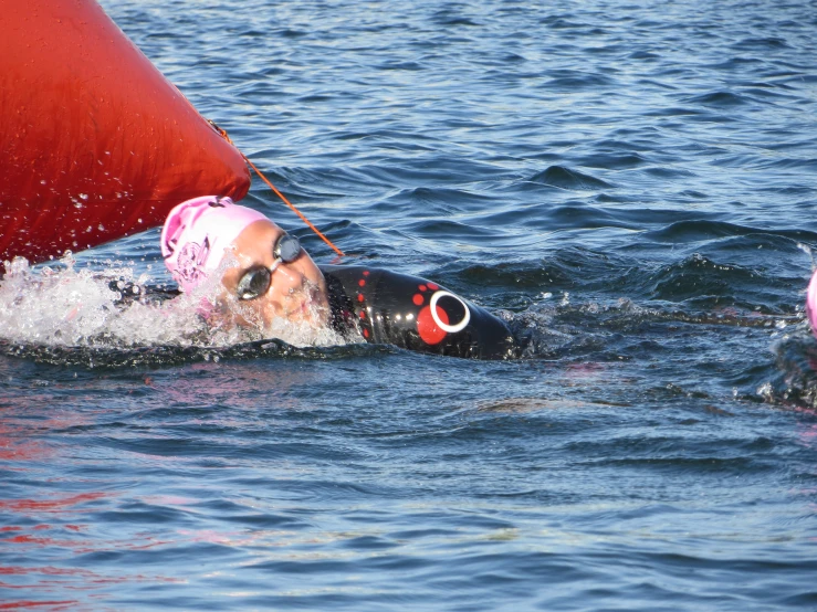 a woman swimming in water next to a red sail boat