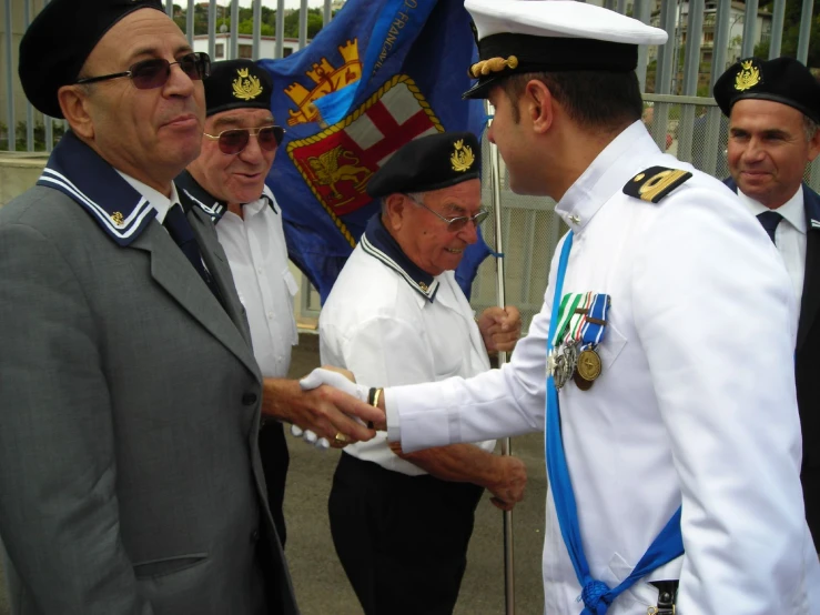four men in white suits shake hands next to flags
