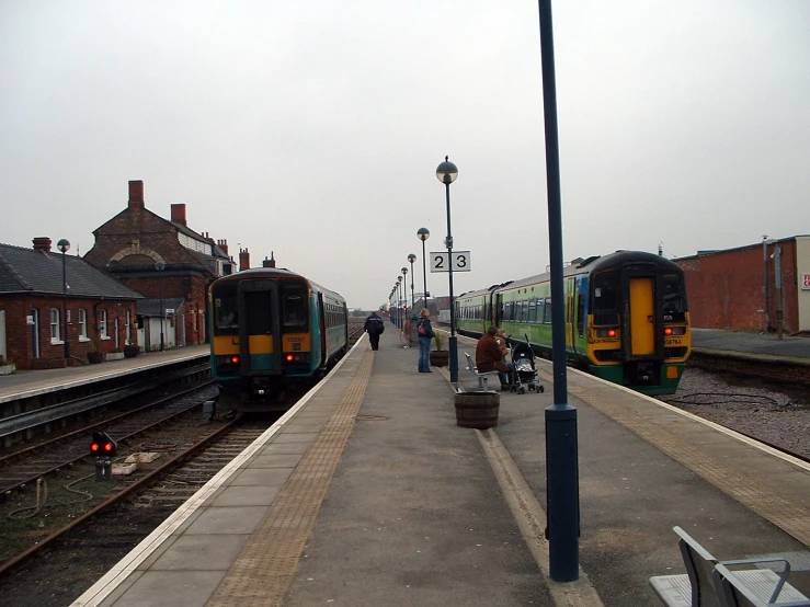 two trains pulled into a train station with people walking about