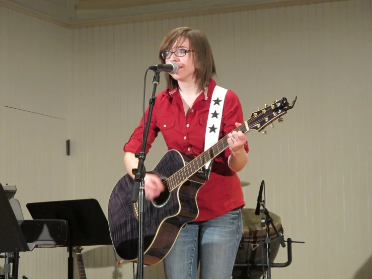 woman with eyeglasses playing guitar on stage