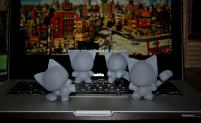 three small plastic toy cats sit on the keyboard of an open laptop computer