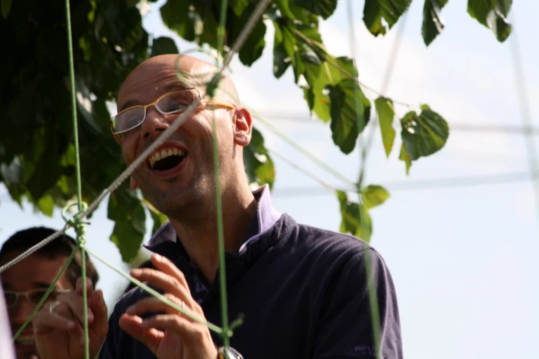 two men stand behind the green leaves of a tree