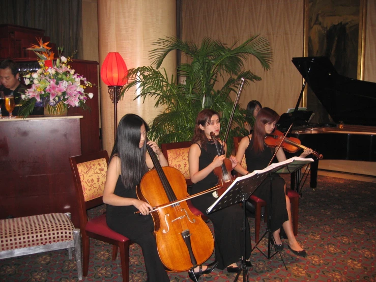 two women sitting in chairs with cellos, a piano and flowers