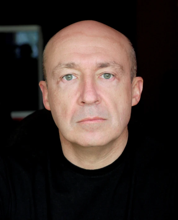 a man with a black t - shirt stares at the camera