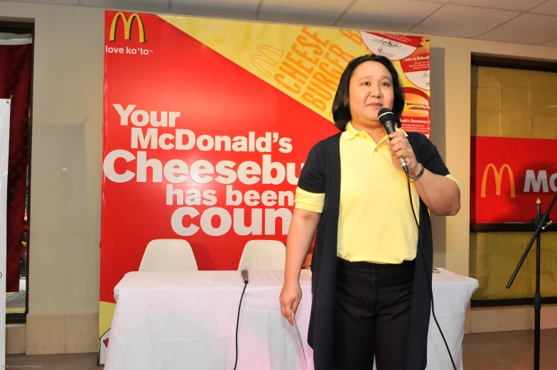 woman standing in front of mcdonald's advertising sign, microphone in hand