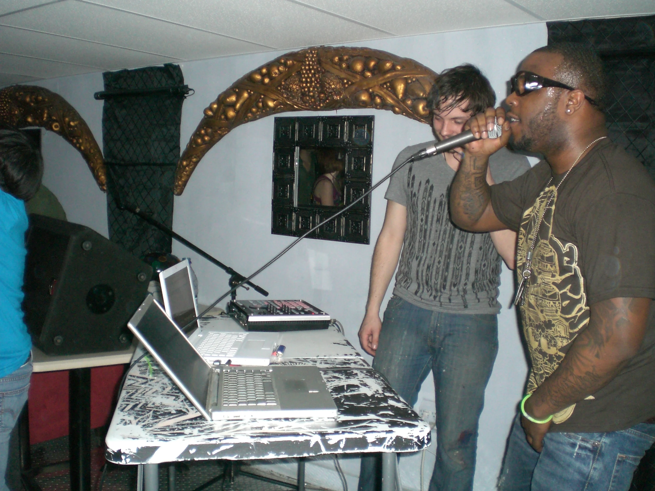 two men singing into microphones in front of an open laptop