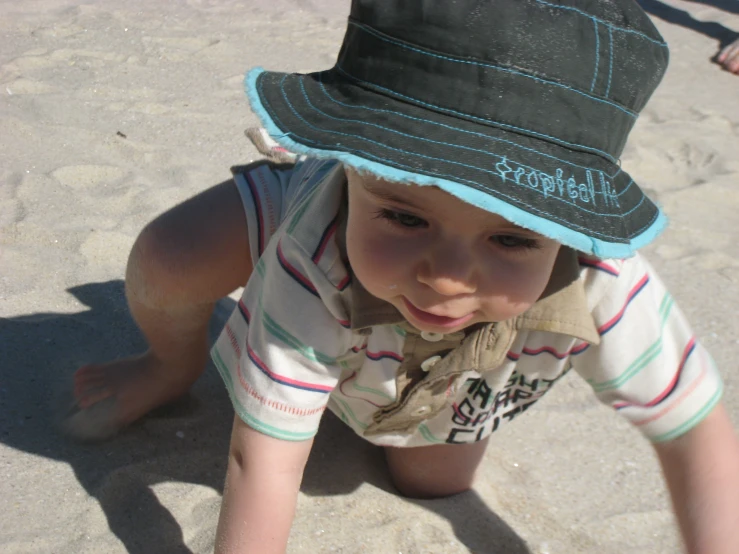 the child wearing a hat is sitting on the beach