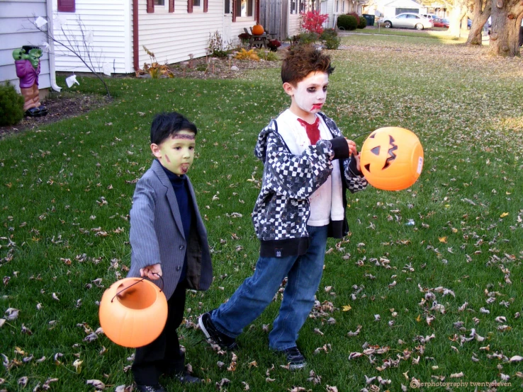 two boys are standing in a yard holding pumpkins