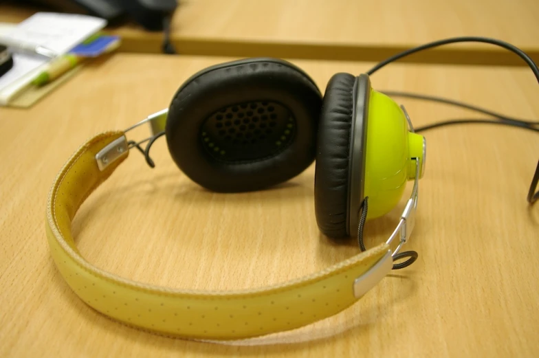 yellow headphones and black earbuds lying on top of a wooden desk