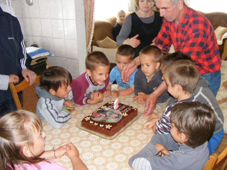 a man and five children looking at a chocolate birthday cake