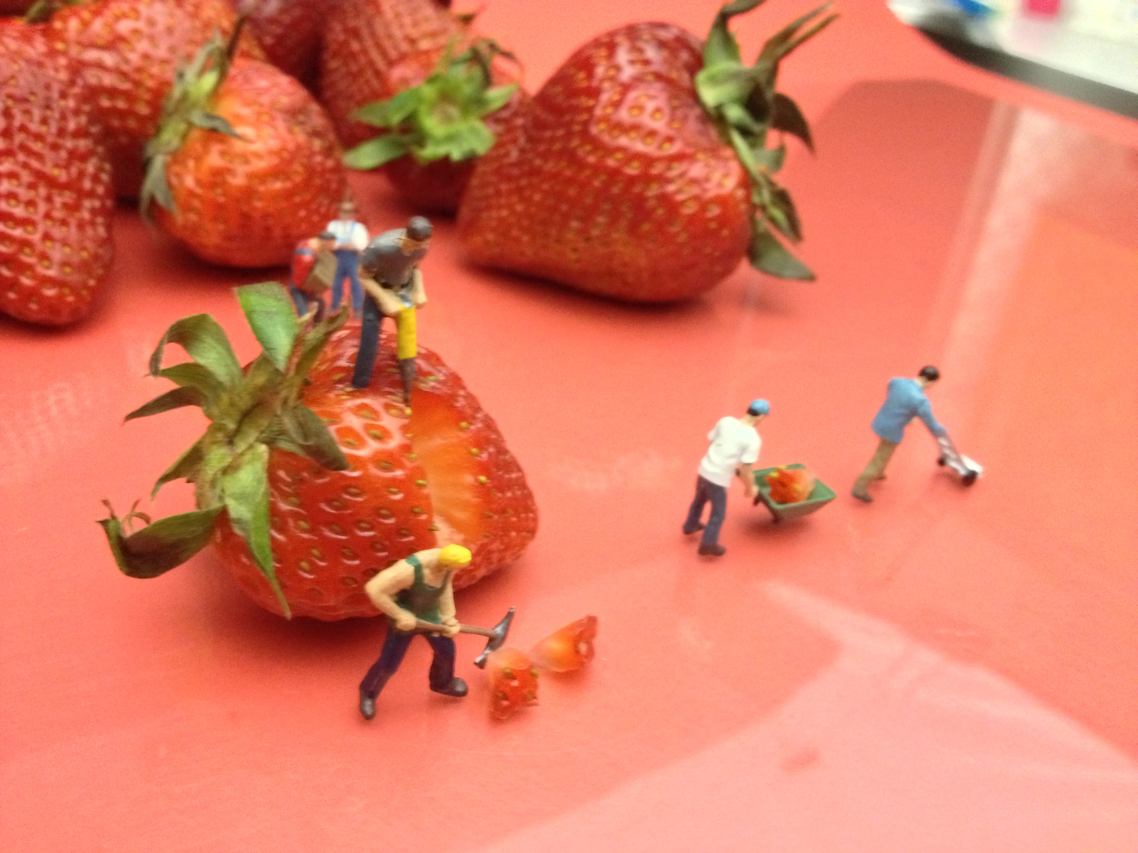 a group of toy people stand next to strawberries on a surface