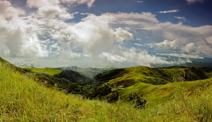 this is a grassy hillside with mountains and clouds