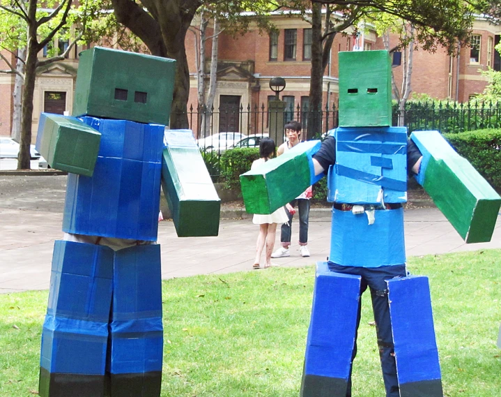 two cardboard man stand in the grass holding up their arms